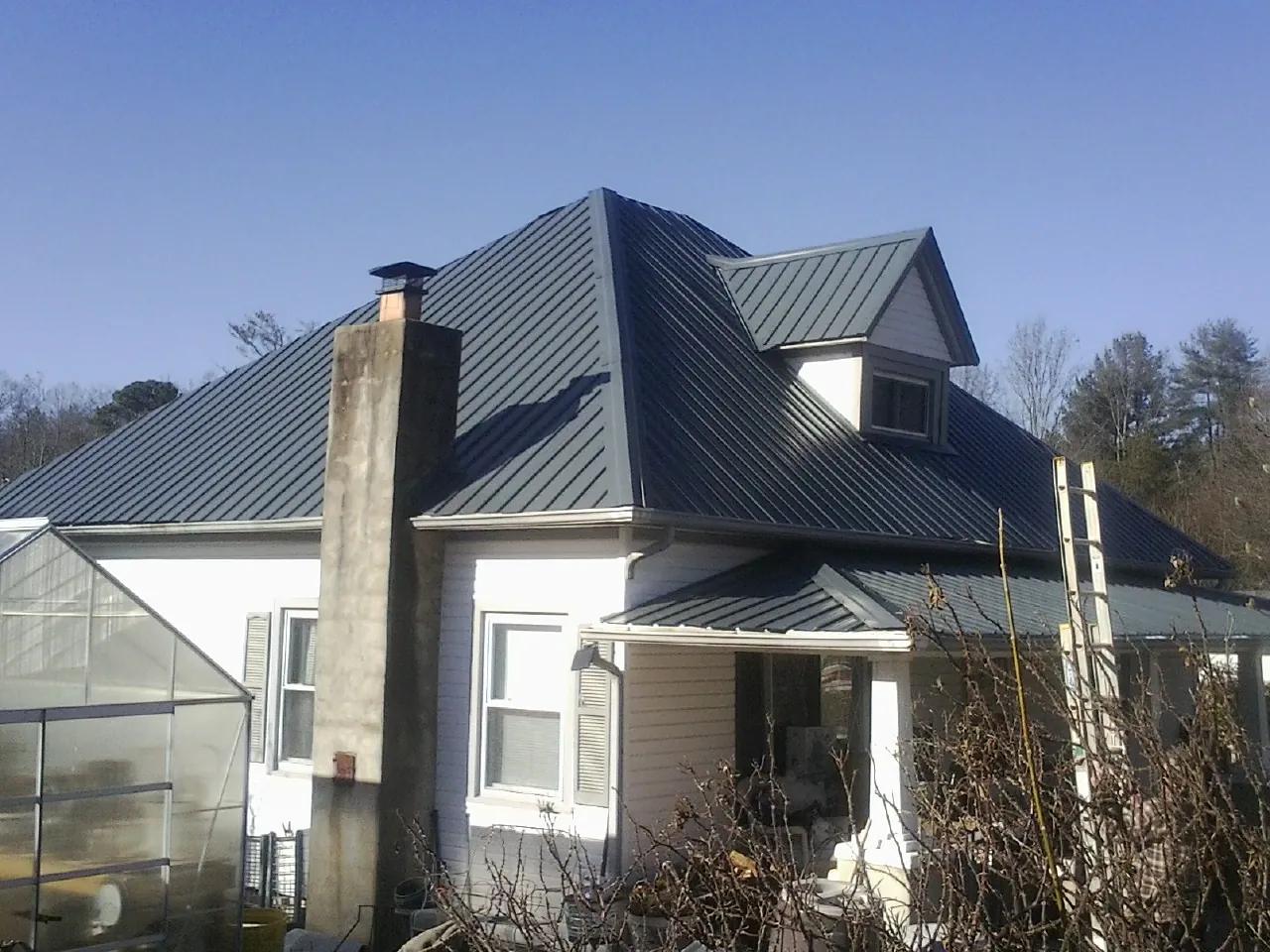 Dark blue standing seam metal roof on a white farmhouse with dormer — Slate & Tile Roof Repair by Roofing Brothers in Loughman