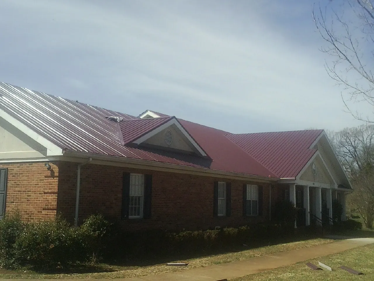 Red metal roof with gabled entries on a long brick building, from a Hail Damage Roof Repair job in Loughman
