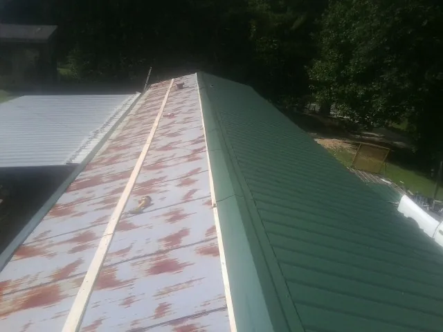 Old rusted panels beside newly installed green metal roofing — Wind Damage Roof Repair by Roofing Brothers in Loughman