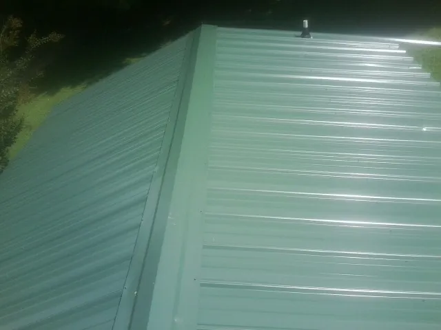 New green metal panels meeting at the ridge of a roof — Flat Roof Repair work by our crew in Loughman