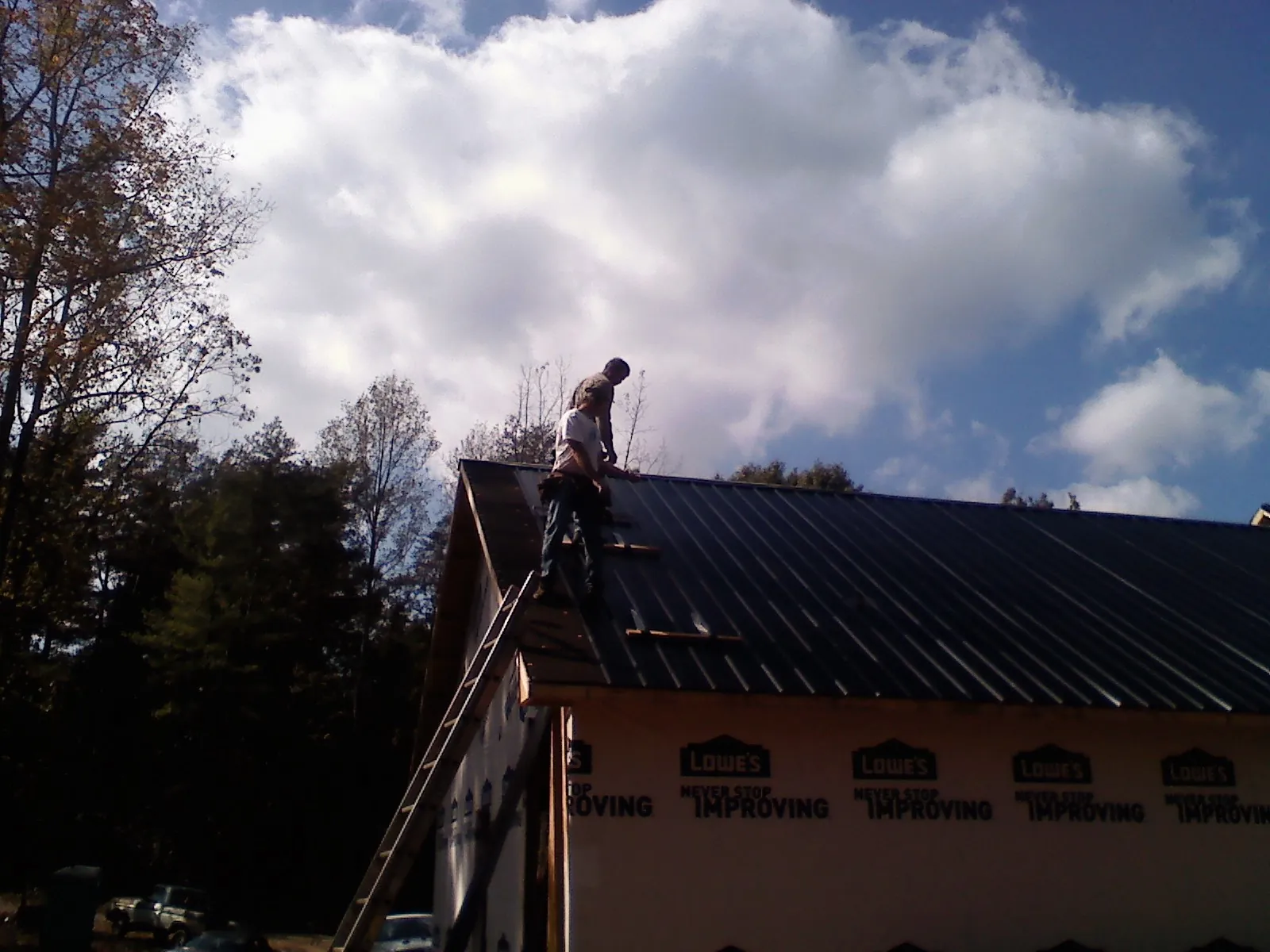 Roofer fastening dark metal panels high against a cloudy sky, from a Roof Inspection job in Loughman