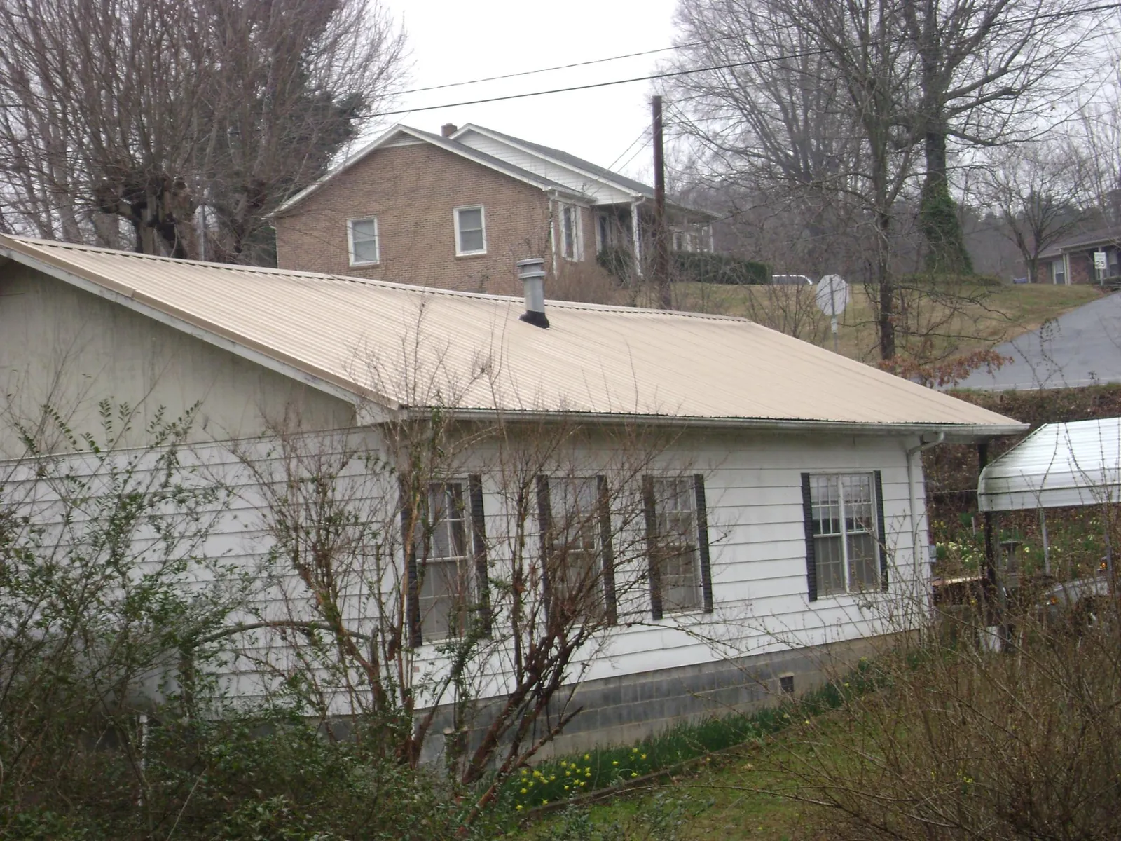 Tan metal roof on a white sided house set into a hillside — Commercial Roofing by Roofing Brothers in Loughman