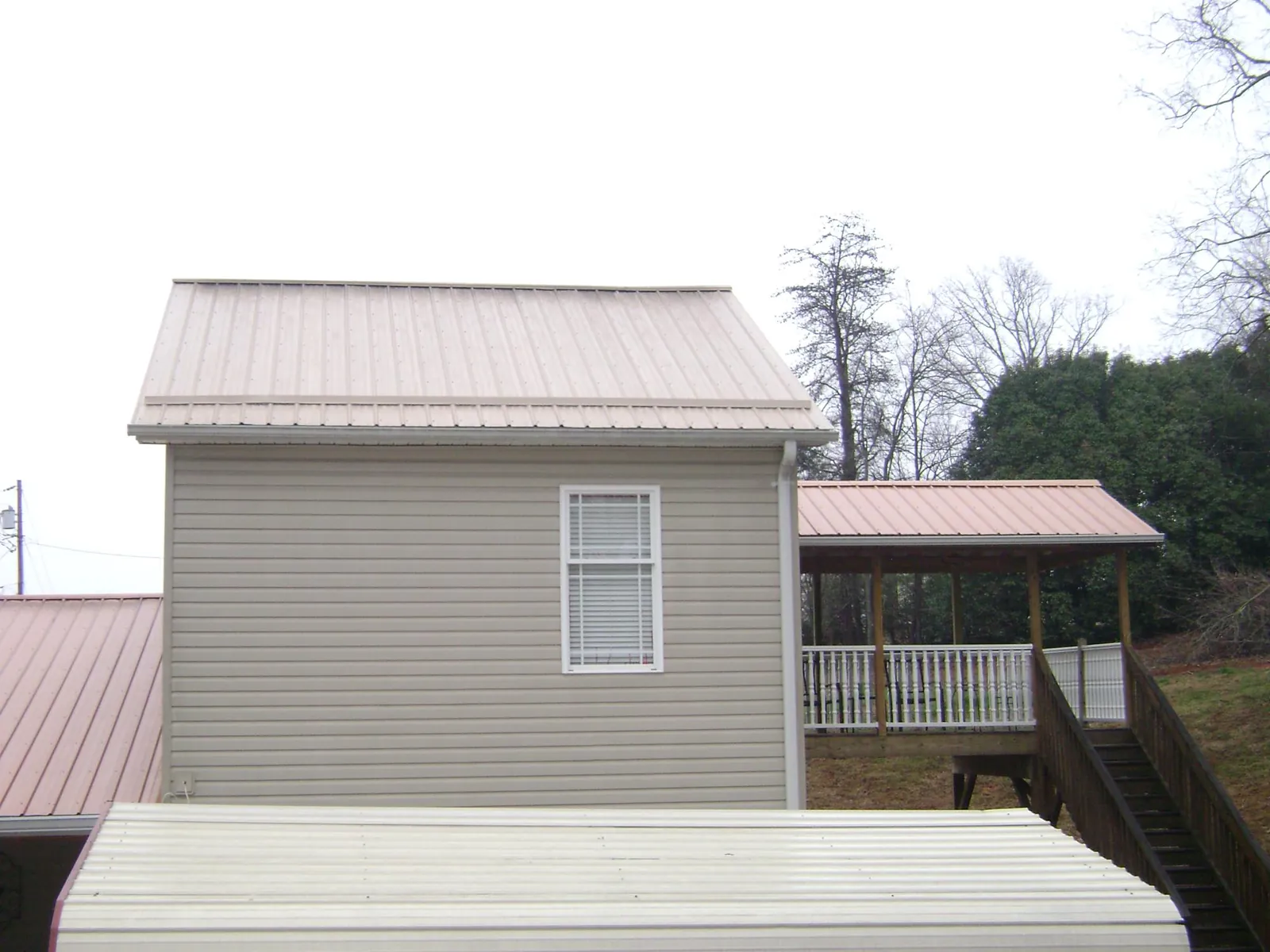 Tan metal roofs on a two story addition and attached porch, from a Roof Replacement job in Loughman